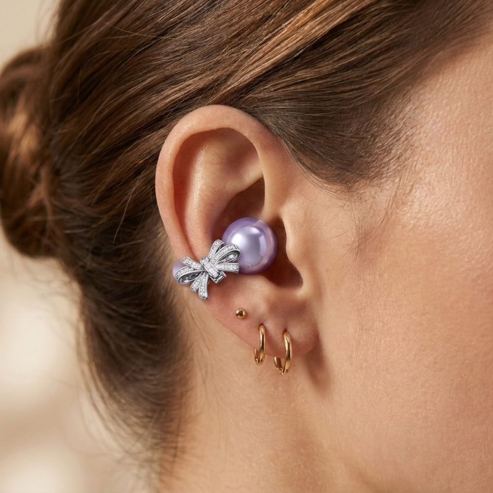 A close-up of a woman's ear with a large lavender pearl earring adorned with a diamond bow.