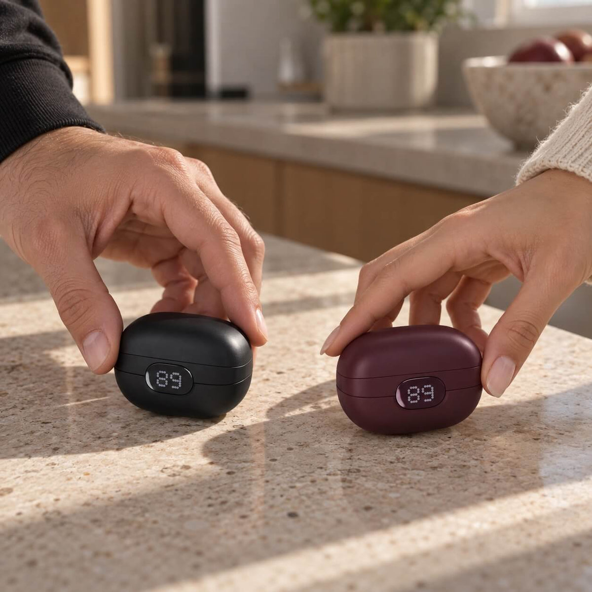 Two hands each picking up a ViSound Ease case, one black and one burgundy, from a kitchen counter