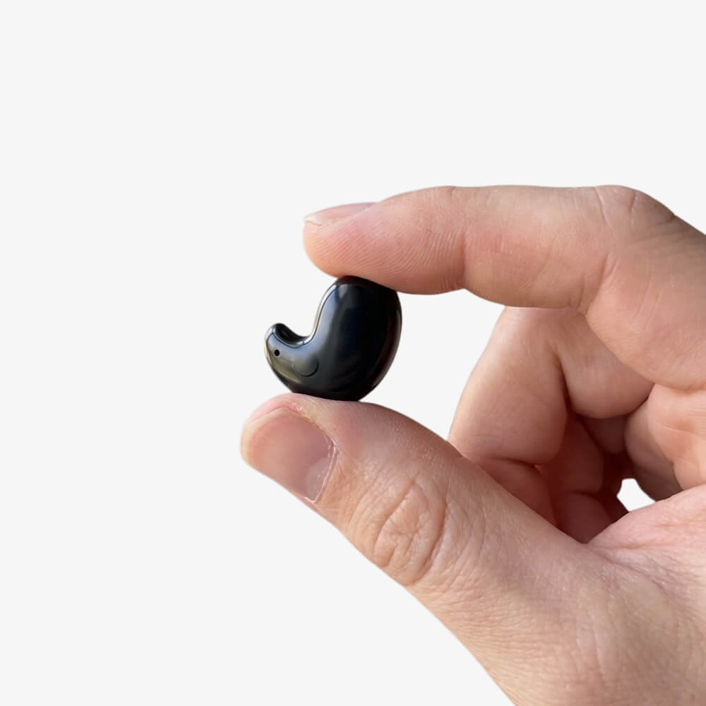 A close-up of a hand holding a tiny, black wireless earbud between two fingers.
